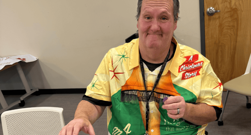 A man in a yellow and green shirt is sitting at a table.