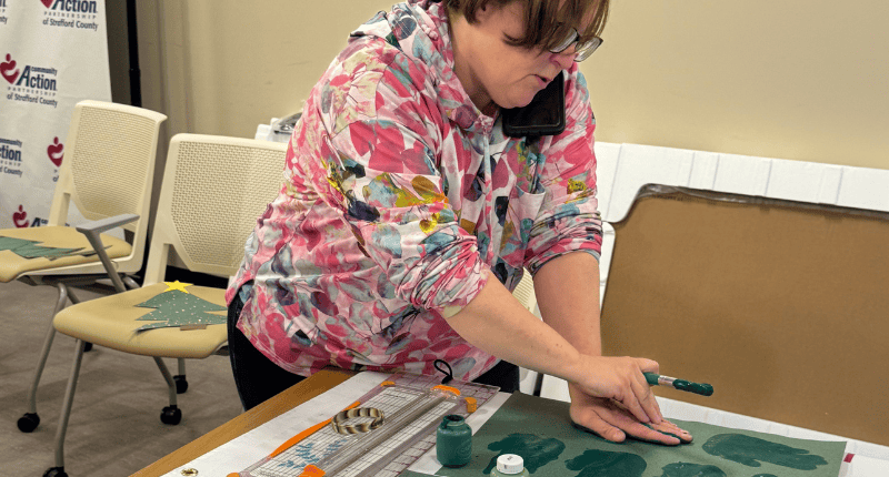 A woman in pink shirt working on green and white painting.